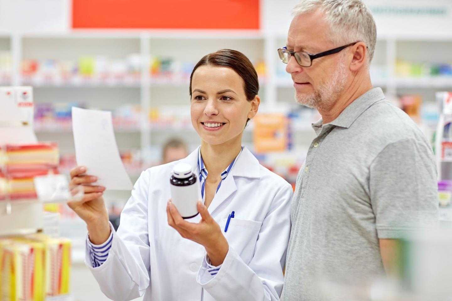 Фармацевт в аптеке показывает мужчине лист и пузырек с лекарством
