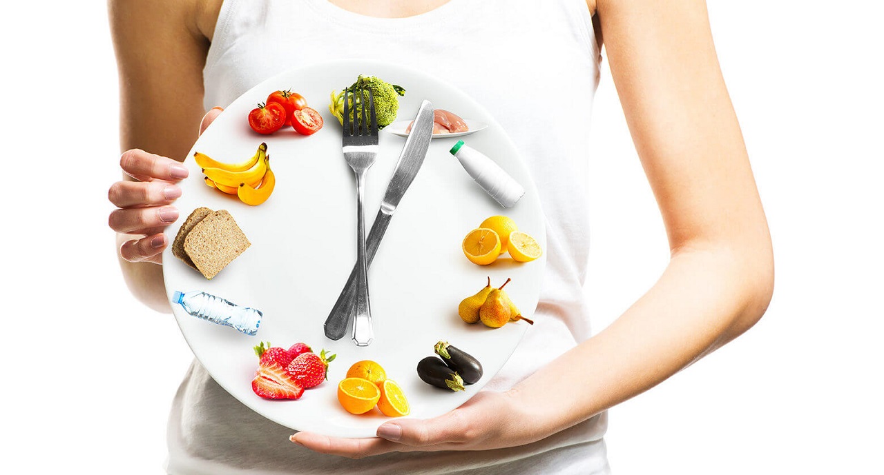 девушка держит тарелку с овощами и фруктами вилкой и ножом